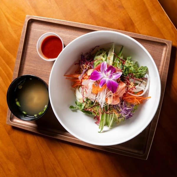 Colorful Japomen sashimi salad with a purple orchid, miso soup, and red sauce on a wooden tray.
