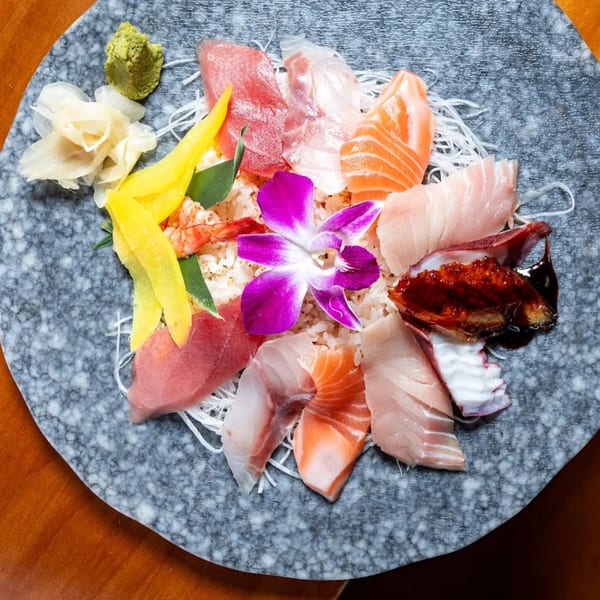 Assorted sashimi and seafood, including tuna, salmon, and octopus, garnished with a purple orchid.
