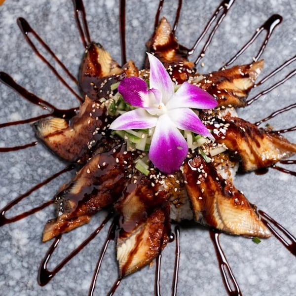 Unagi sushi pieces arranged in a star shape, drizzled with sauce and garnished with a purple orchid.