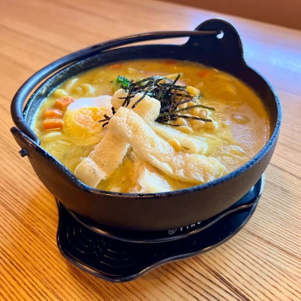 Japomen curry ramen in a black pot, topped with egg, carrots, corn, seaweed, and fried tofu.