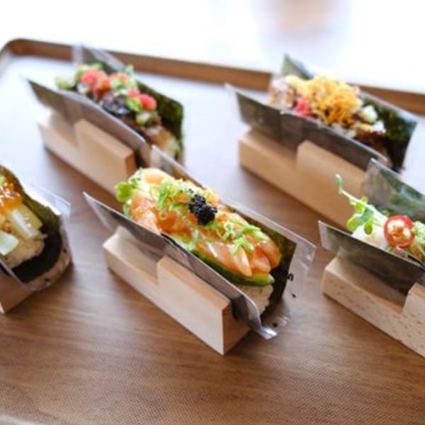 A wooden tray holds several Japomen hand rolls, each with different toppings like salmon, avocado, and caviar.