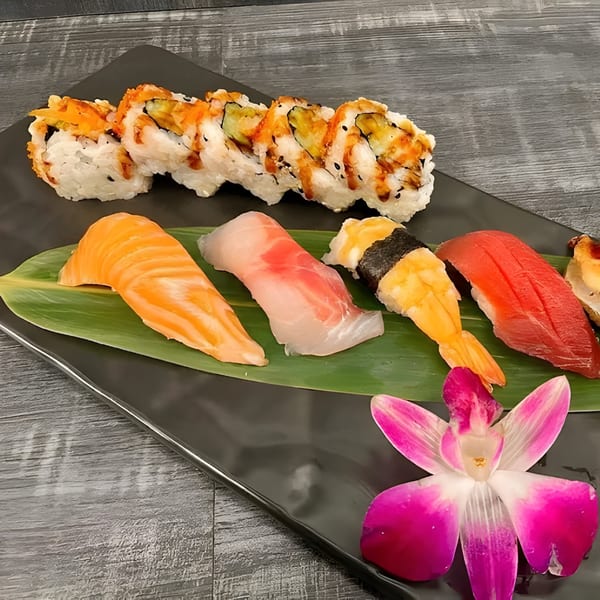 A black plate with sushi rolls, nigiri, and a pink orchid on a banana leaf.